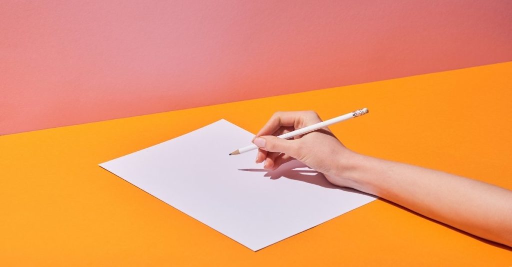 Ymmärrettävä kieli -artikkelin kuvituskuva: Henkilön käsi kirjoittamassa lyijykynällä valkoiselle A4-paperille. 